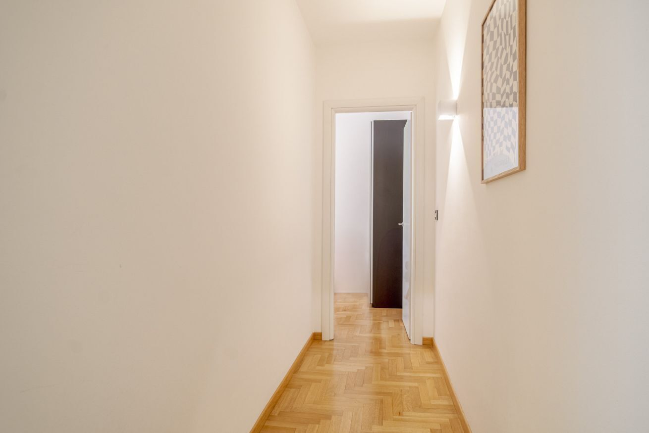 A hallway with a wooden floor, white walls, and a door at the end.
