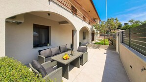 A covered outdoor seating area with wicker furniture and a table, surrounded by a low wall and a tree. - 1 bedroom beautiful apartment in Muntic (Muntic)