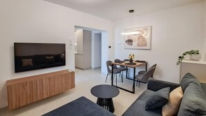 A modern living room with a flat-screen TV, a wooden cabinet, a sofa, a dining area with chairs, and a small table. - 1 bedroom beautiful apartment in Muntic (Muntic)