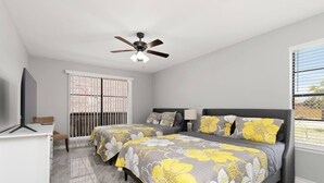 A bedroom with two beds, a desk, a ceiling fan, and a window with blinds. - The 3 Queen Modern by 802 & Paredes (Brownsville)
