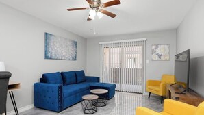 A modern living room with a blue sectional sofa, yellow armchairs, and a ceiling fan. - The 3 Queen Modern by 802 & Paredes (Brownsville)