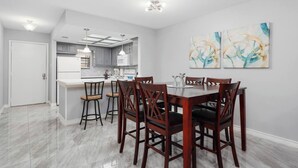 A modern kitchen with grey cabinets, a white refrigerator, and a dining area with a wooden table and chairs. - The 3 Queen Modern by 802 & Paredes (Brownsville)