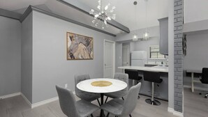 Eine moderne Küche mit weißen Geräten, eine Essecke mit einem runden Tisch und grauen Stühlen sowie ein großes abstraktes Gemälde an der Wand.