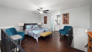 Ein geräumiges Schlafzimmer mit einem großen Bett, zwei Sesseln, einer Bank, einem Deckenventilator und einer Treppe.