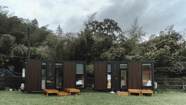 Two modern, dark wooden cabins with glass doors, each featuring a small wooden table and bench. - Jade in the Wilderness (碧野寮) (Dahu Township)