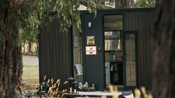 Une petite cabane au revêtement extérieur en bois, avec une porte et une enseigne sur laquelle on peut lire : « Charmant et minuscule ».