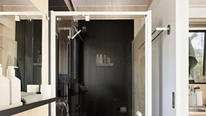 A modern bathroom with a glass-enclosed shower, a white sink, and a wooden vanity. - Delightfully Tiny by Tiny Away (Springmount)