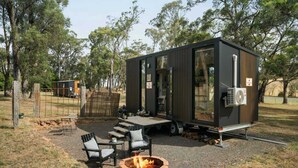 A modern, compact cabin with a fire pit and outdoor seating, surrounded by trees. - Delightfully Tiny by Tiny Away (Springmount)