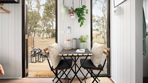 A modern outdoor dining area with a table and chairs, a hanging plant, and a view of the outdoors. - Charmingly Tiny by Tiny Away (Springmount)