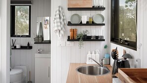 A modern kitchen with white wooden paneling, a stainless steel sink, and black shelves holding dishes and kitchen items. - Charmingly Tiny by Tiny Away (Springmount)