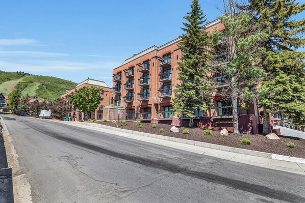 A multi-story hotel with balconies, a landscaped front yard, and a hilly backdrop.