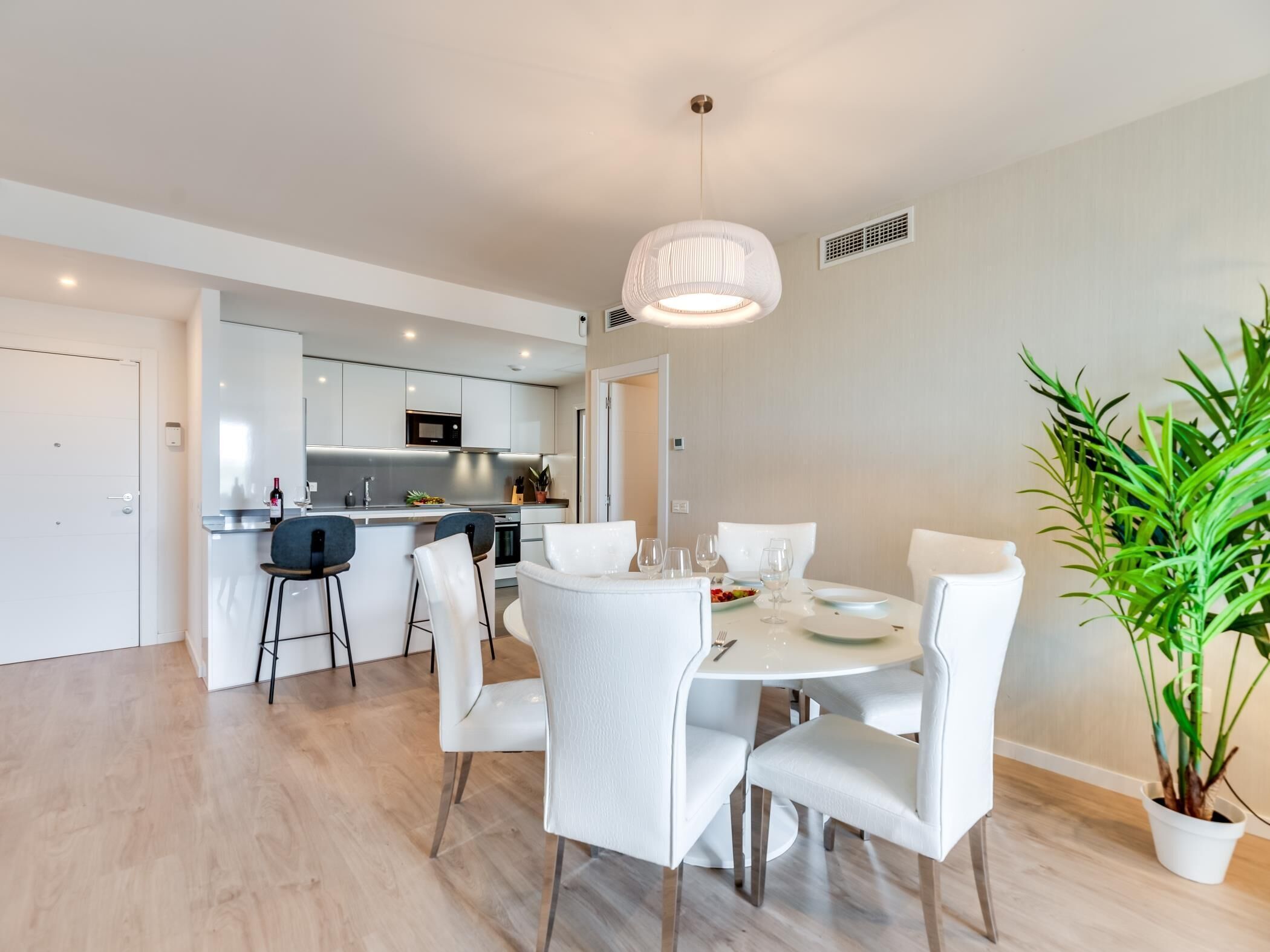 A modern kitchen with white cabinets, a central island, and a dining area with a round table and white chairs.