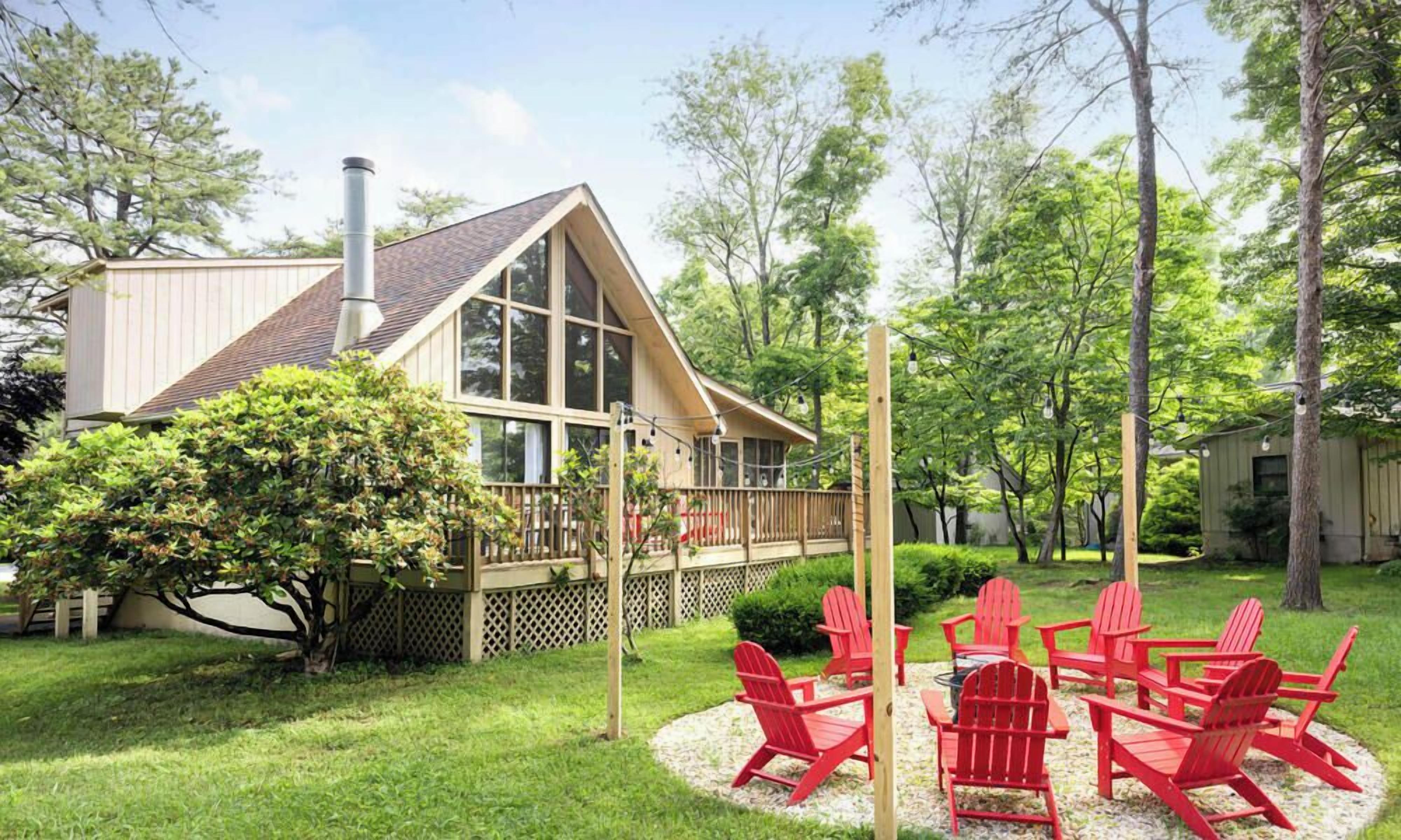 A house with a deck, a chimney, and a garden with red chairs.
