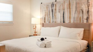 Un lit bien fait, avec du linge de lit blanc et une serviette enroulée, ornée d’un ruban noir.