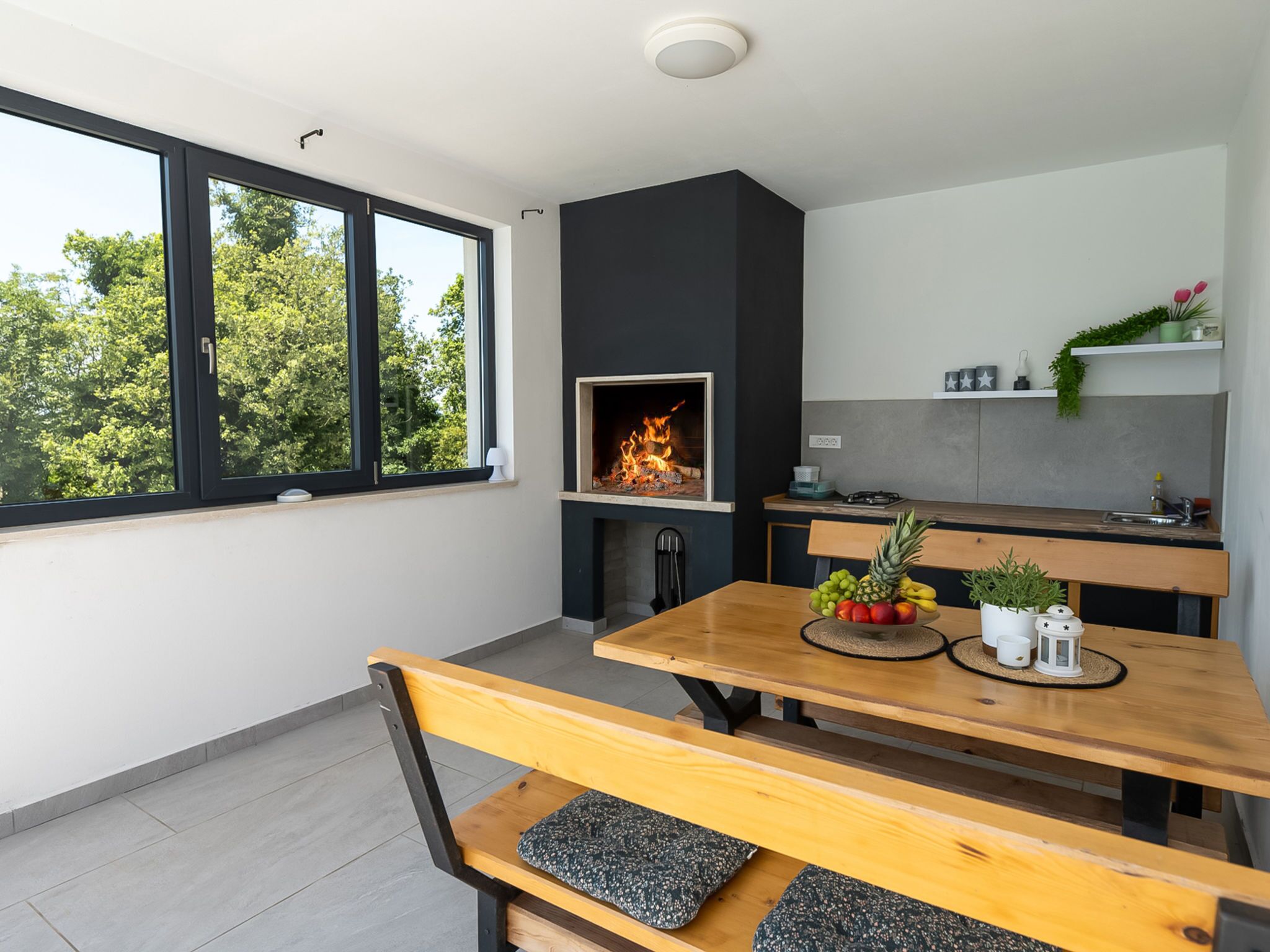 A modern kitchen with a built-in fireplace, a dining table with benches, and a view of trees through large windows.