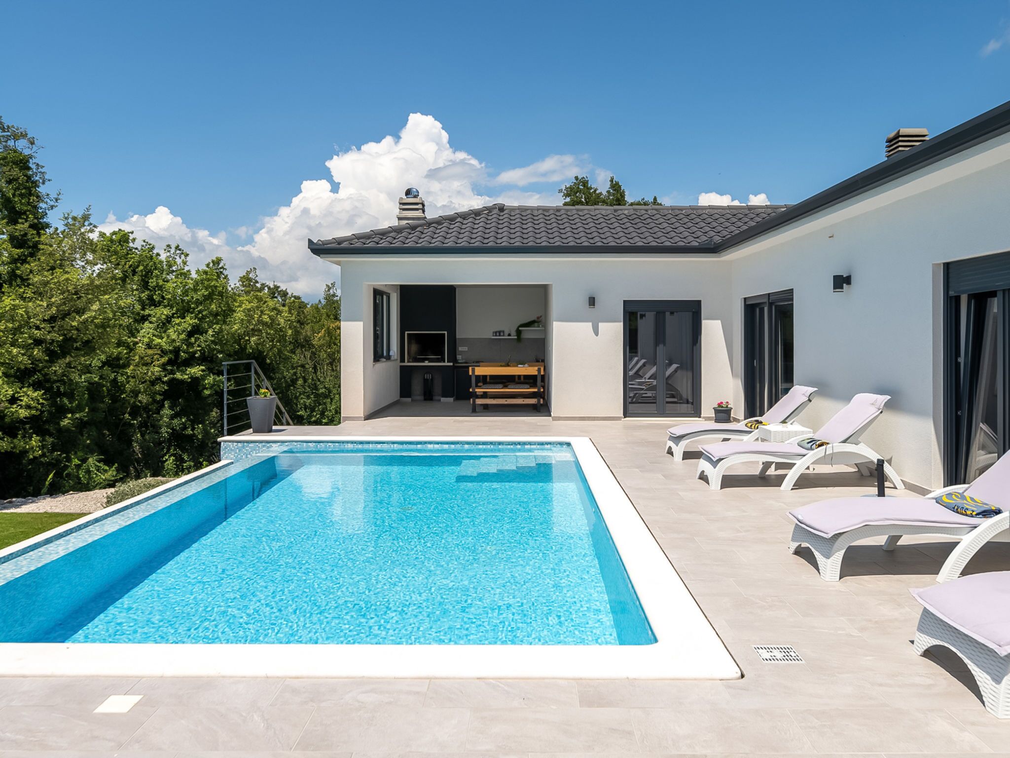 Una casa moderna con piscina, comedor y patio con sillones de descanso.