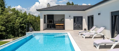 A modern house with a swimming pool, a dining area, and a patio with lounge chairs.