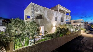 Un bâtiment moderne à plusieurs étages, doté d’un toit plat et de grandes fenêtres, entouré de verdure et d’un mur de pierre.
