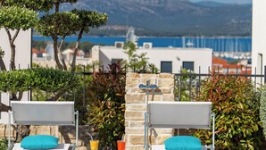 Un espace aménagé au bord de la piscine, avec deux chaises longues, une petite table avec des boissons, et une vue sur la mer et les montagnes.