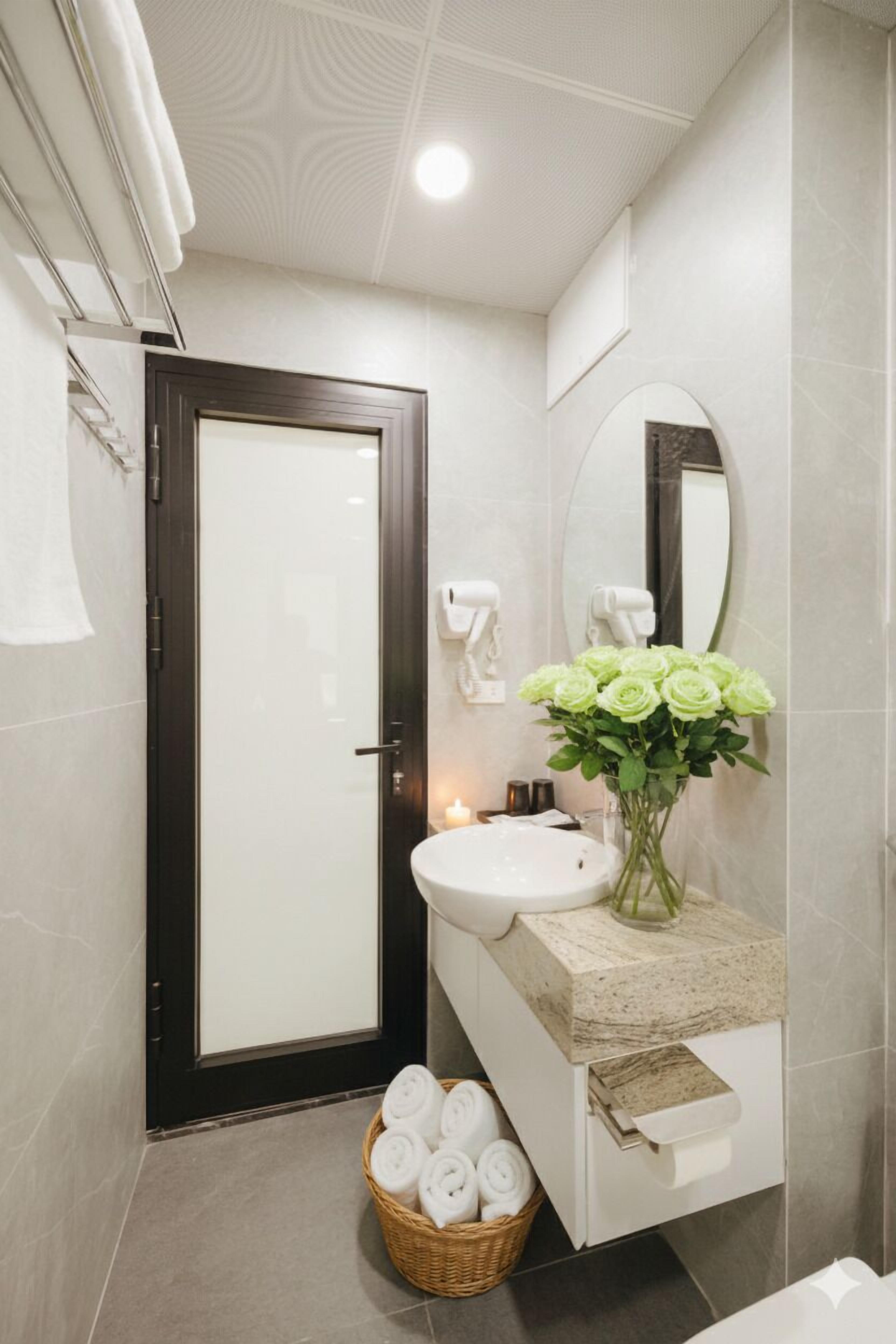 Une salle de bain moderne avec une porte en bois foncé, un lavabo blanc, un miroir et un panier rempli de serviettes pliées.