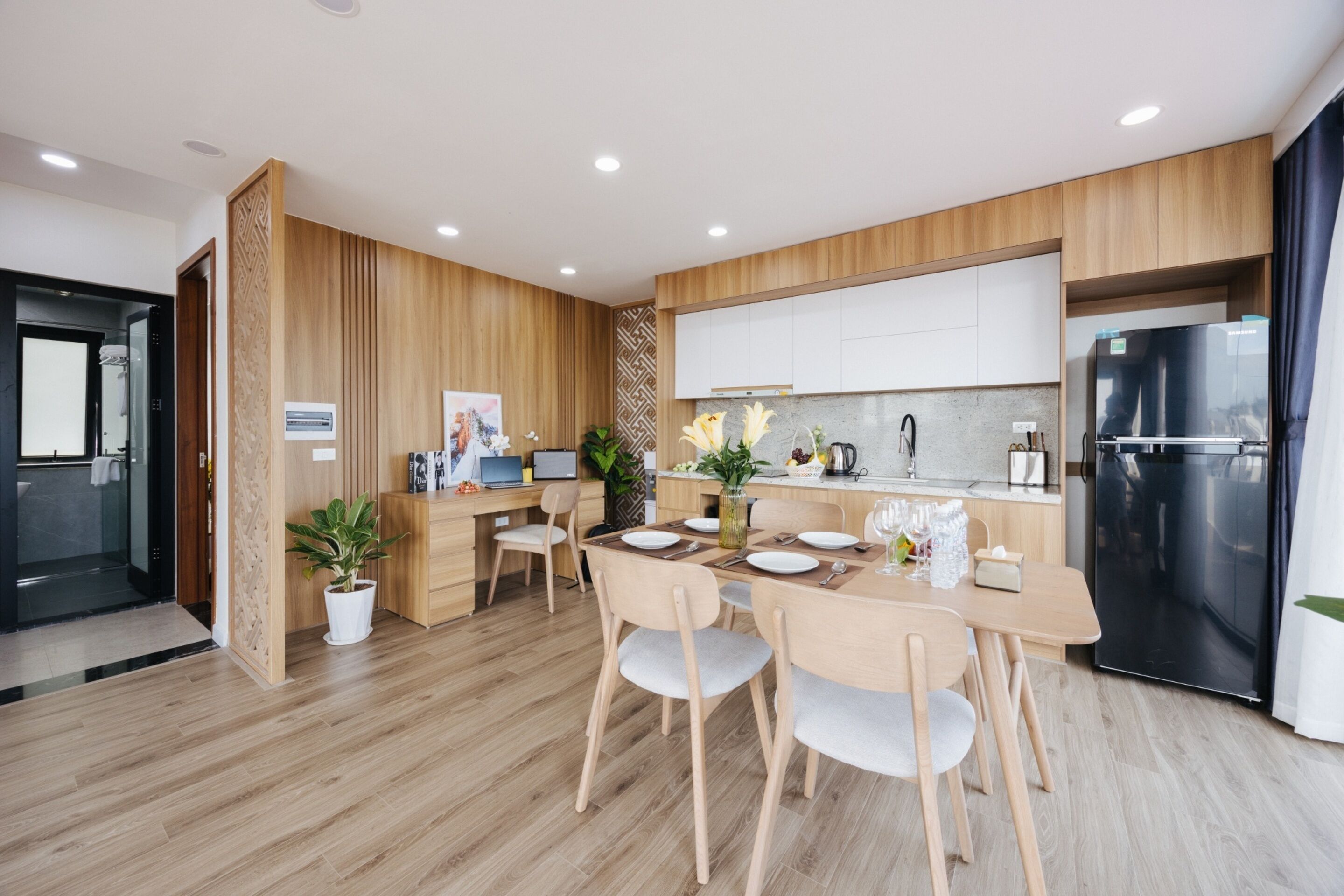 Una cocina moderna con armarios de madera, un comedor con una mesa dispuesta para cuatro personas y un refrigerador negro.