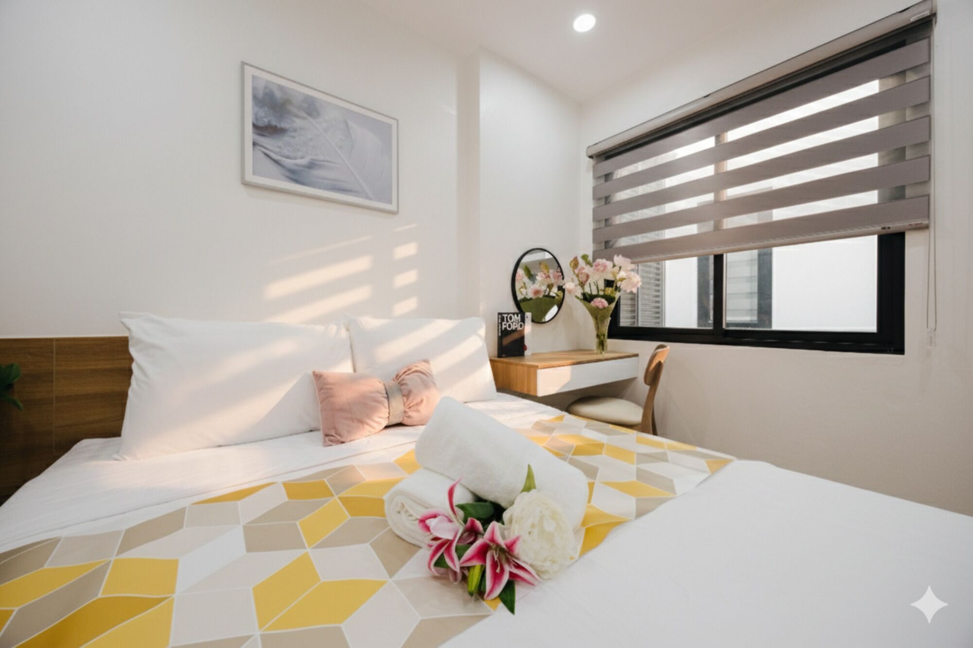 Quarto de hotel com uma cama, uma escrivaninha, uma cadeira, uma janela com persianas, um quadro na parede e um arranjo de flores sobre a cama.
