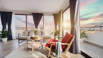 A modern living room with a sofa, a red chair, a coffee table, and a view of the cityscape at sunset.