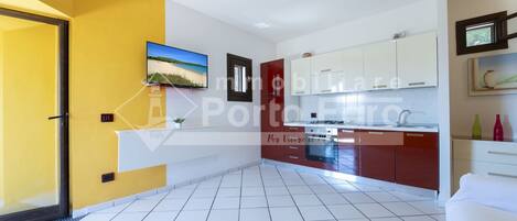 A modern kitchen with white and red cabinets, a built-in oven, and a tiled floor.