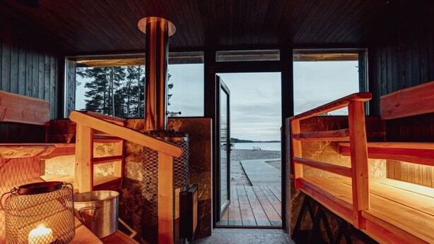 L’intérieur d’un chalet en bois, avec une cheminée, des bancs et une vue sur la plage.