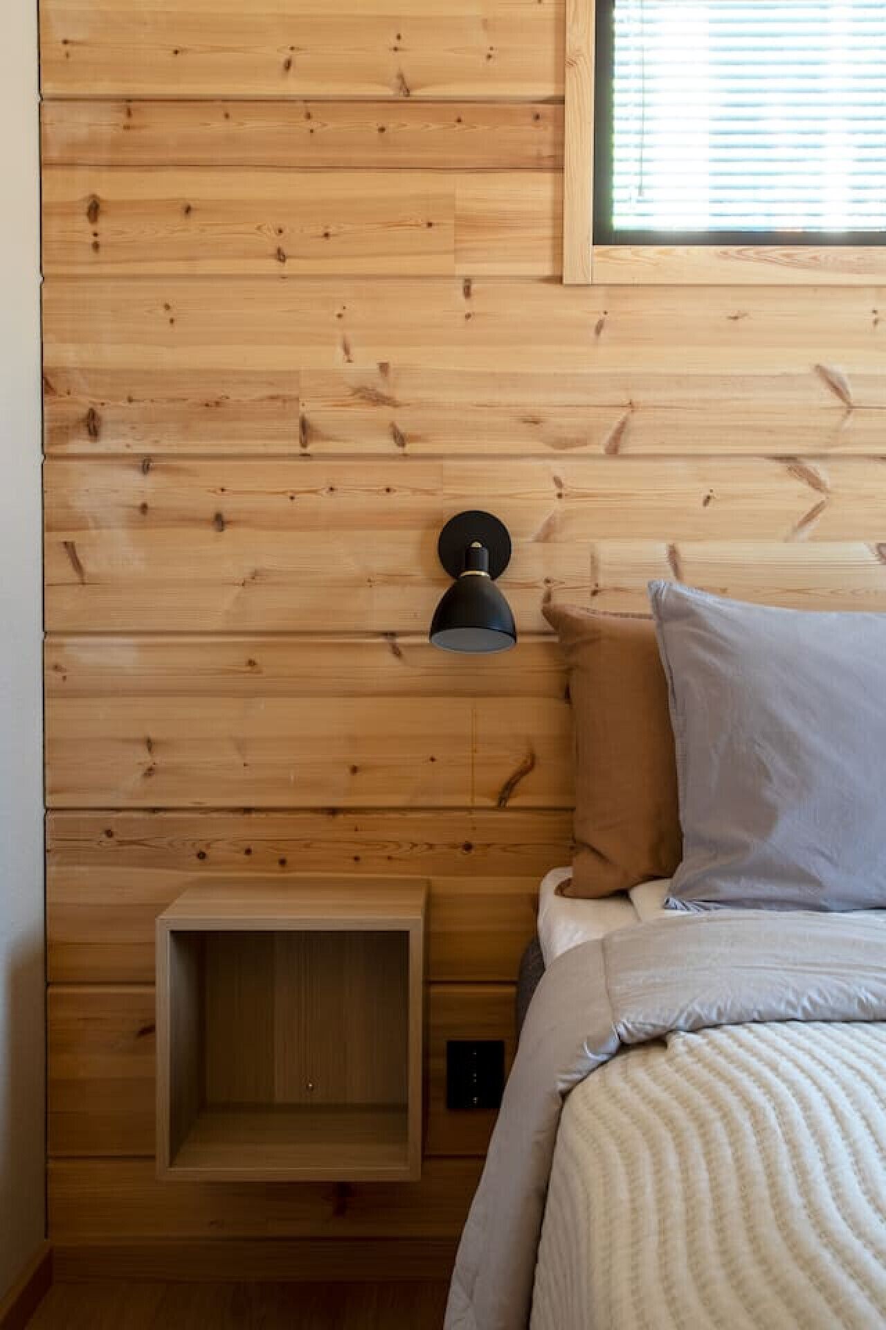 A wooden-paneled room with a bed, a nightstand, and a wall-mounted light fixture.