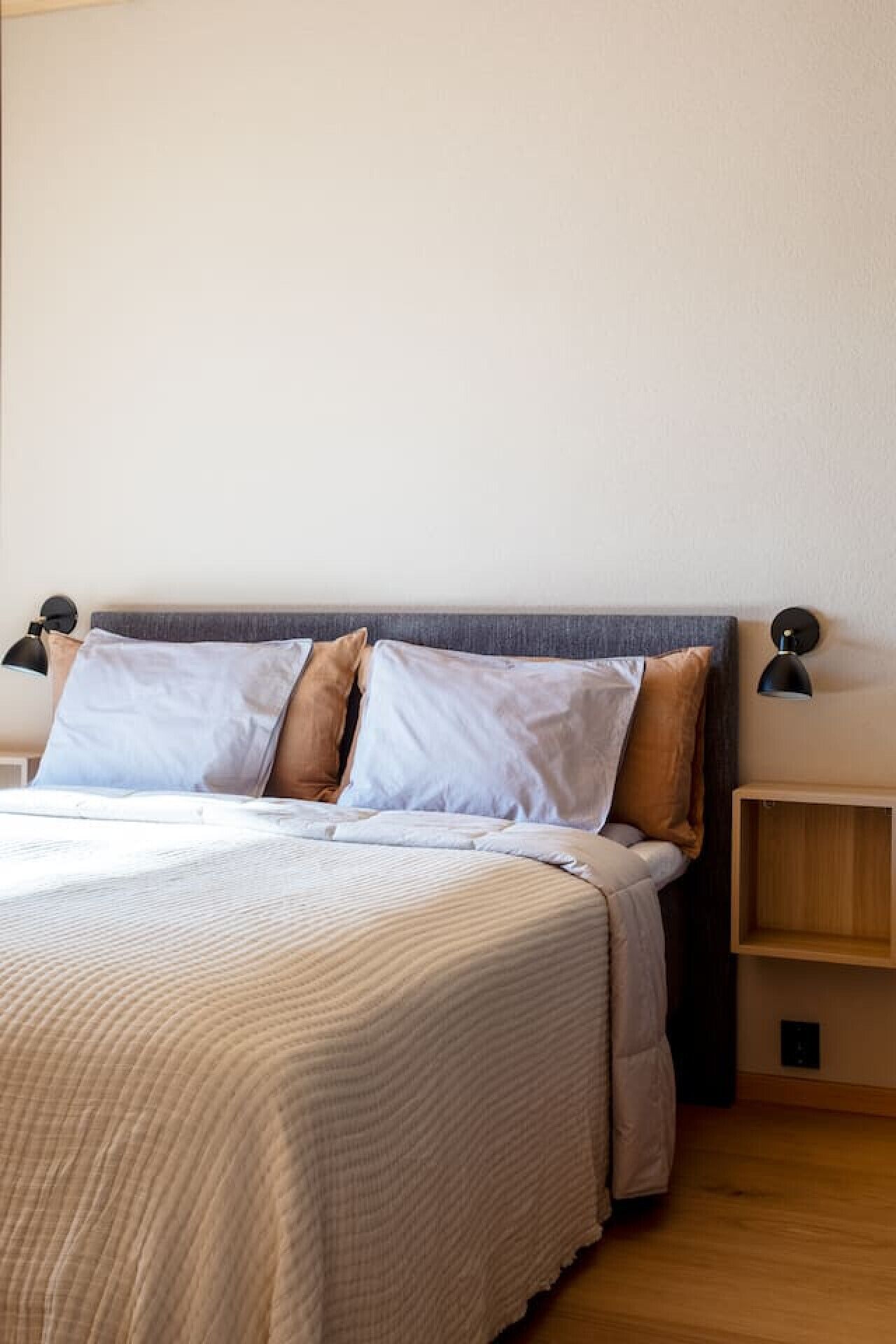 A neatly made bed with a grey headboard, two bedside tables with lamps, and a wooden nightstand.