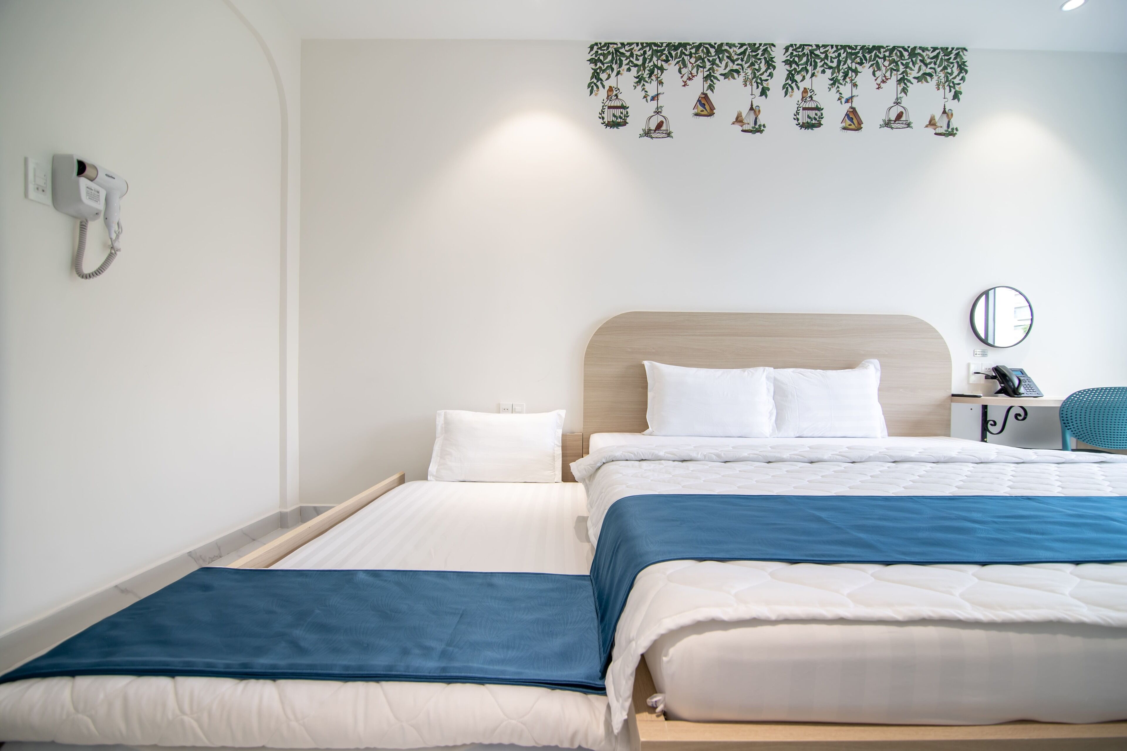 Un letto matrimoniale con biancheria da letto bianco e blu, una testiera in legno, un comodino con il telefono e un telefono fissato al muro.