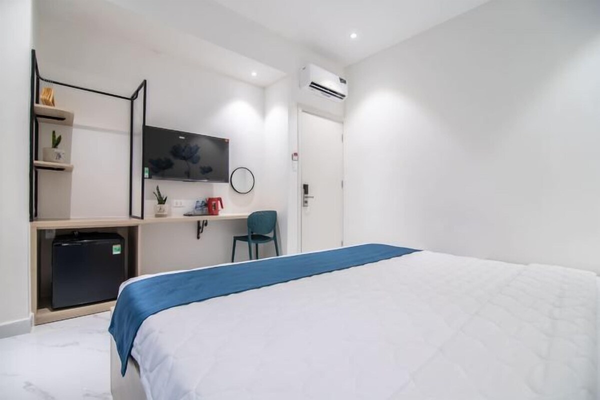 A modern hotel room with a bed, a desk, a chair, a TV, and an air conditioning unit.