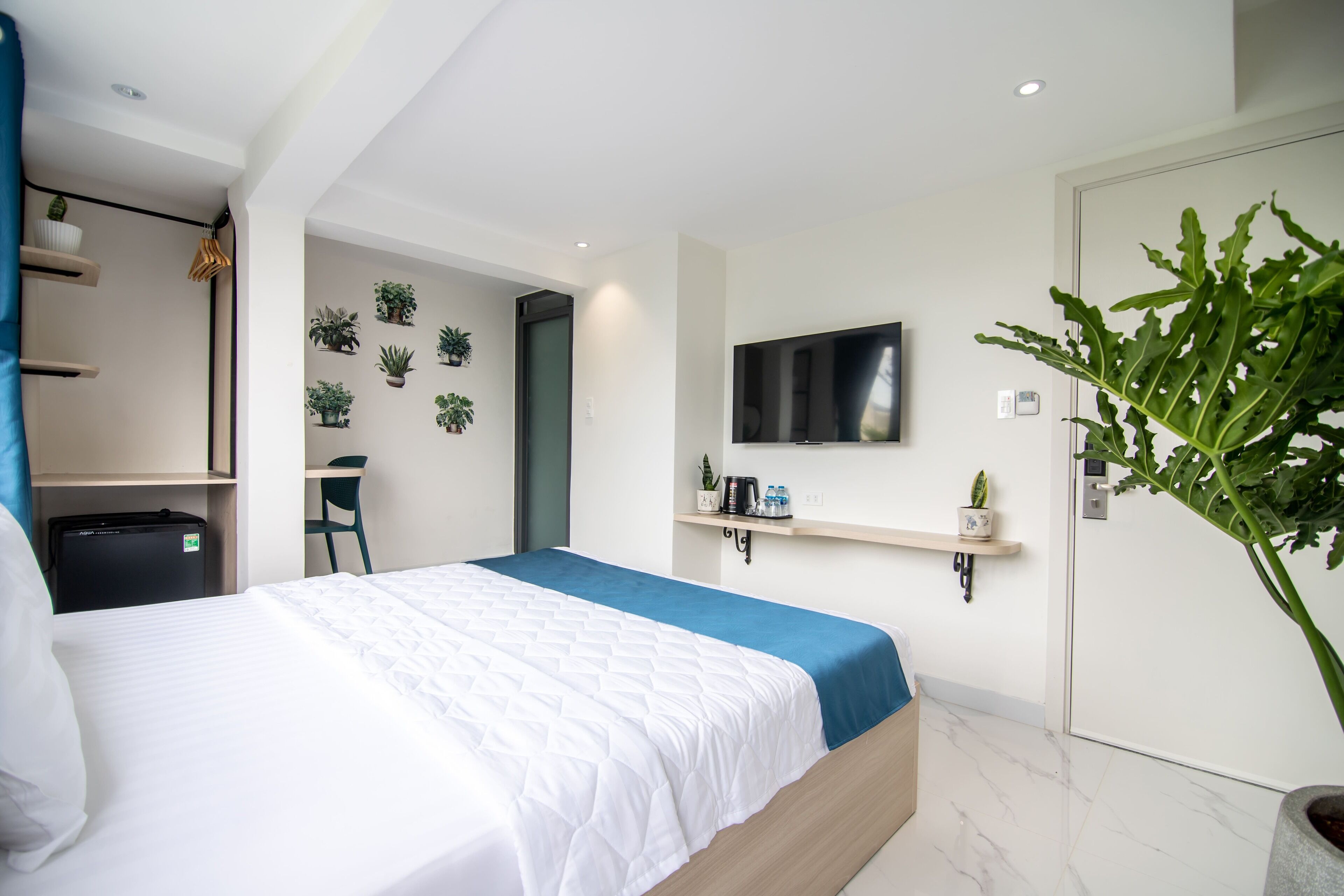 A modern hotel room with a bed, a desk, a TV, and wall-mounted shelves with plants.