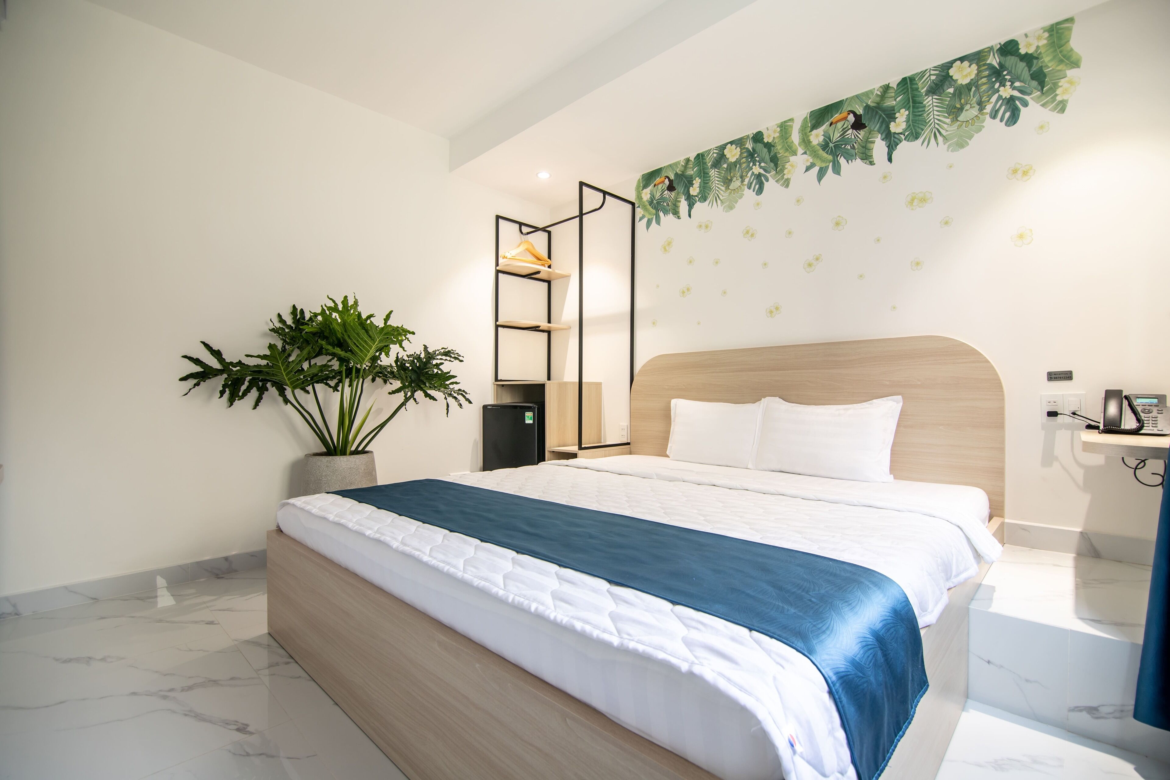 Una habitación de hotel moderna con una cama grande, una planta en maceta, un estante montado en la pared y un mural decorativo.