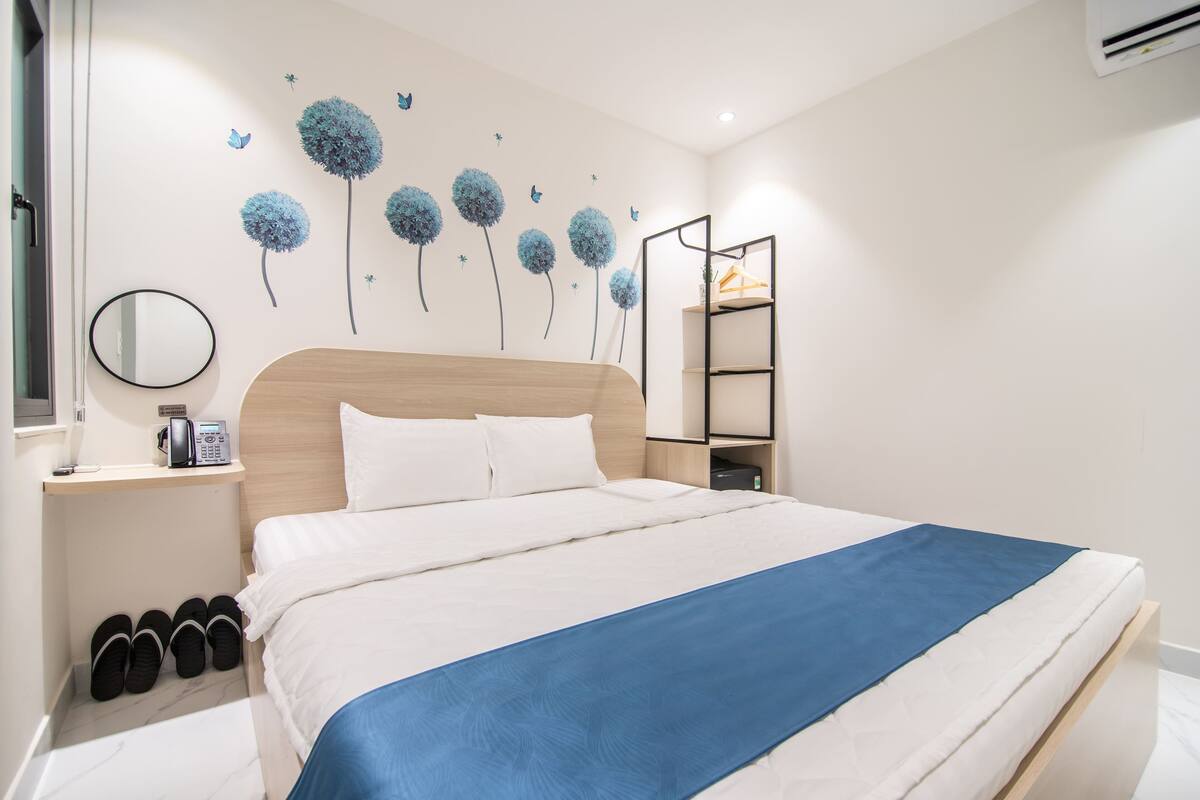 Ein aufgeräumtes Schlafzimmer mit einem Bett, einem Nachttisch, einem Spiegel, einem Regal und einer Wanddekoration.