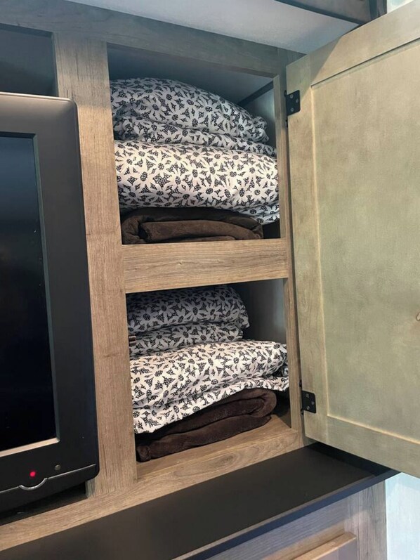 A storage cabinet with multiple shelves containing folded bedding and a television on the left.