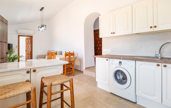 A modern kitchen with white cabinets, a built-in washing machine, and a large island with stools. - Beach front home in Benajarafe (Benajarafe)