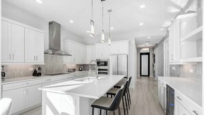 Una cocina moderna con muebles blancos, una isla central con taburetes y una campana extractora de acero inoxidable.
