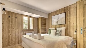 Quarto com cama grande, paredes de madeira, janela e um quadro pendurado.