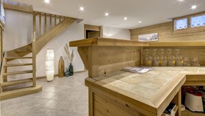 Interior de madeira com escada, área de cozinha com bancada de madeira e janela com vista para árvores.