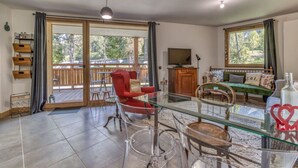 A spacious living room with a glass dining table, red armchair, and a sofa with patterned cushions. - Turra - Cosy 80m2 | Central | Remontée | Parking | Calme (Les Houches)