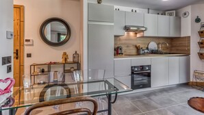 A modern kitchen with white cabinets, a wooden countertop, and a glass dining table. - Turra - Cosy 80m2 | Central | Remontée | Parking | Calme (Les Houches)