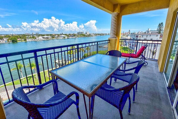 A balcony with a table and chairs, overlooking a river with buildings in the background.