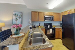 A kitchen with granite countertops, stainless steel appliances, wooden cabinets, and a microwave.