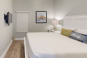 Un dormitorio con cama, una mesita de noche con lámpara, un cuadro enmarcado en la pared y una ventana con persianas.