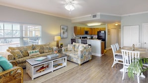 A spacious living room with a sofa, coffee table, and dining area. A kitchen is visible in the background.
