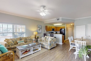 A spacious living room with a sofa, coffee table, and dining area. A kitchen is visible in the background.