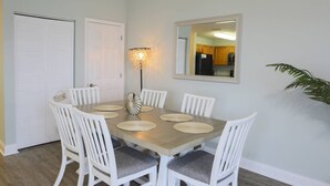 A dining area with a wooden table, white chairs, a wall-mounted mirror, and a floor lamp.