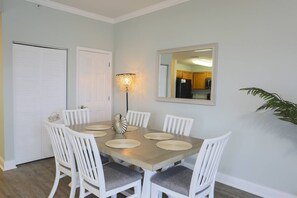 A dining area with a wooden table, white chairs, a wall-mounted mirror, and a floor lamp.